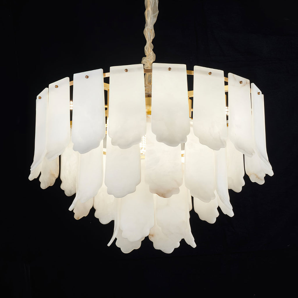 The Clérachic Hue Alabaster Chandelier lit against black, light passing through the stone and pooling behind the lower tiers.