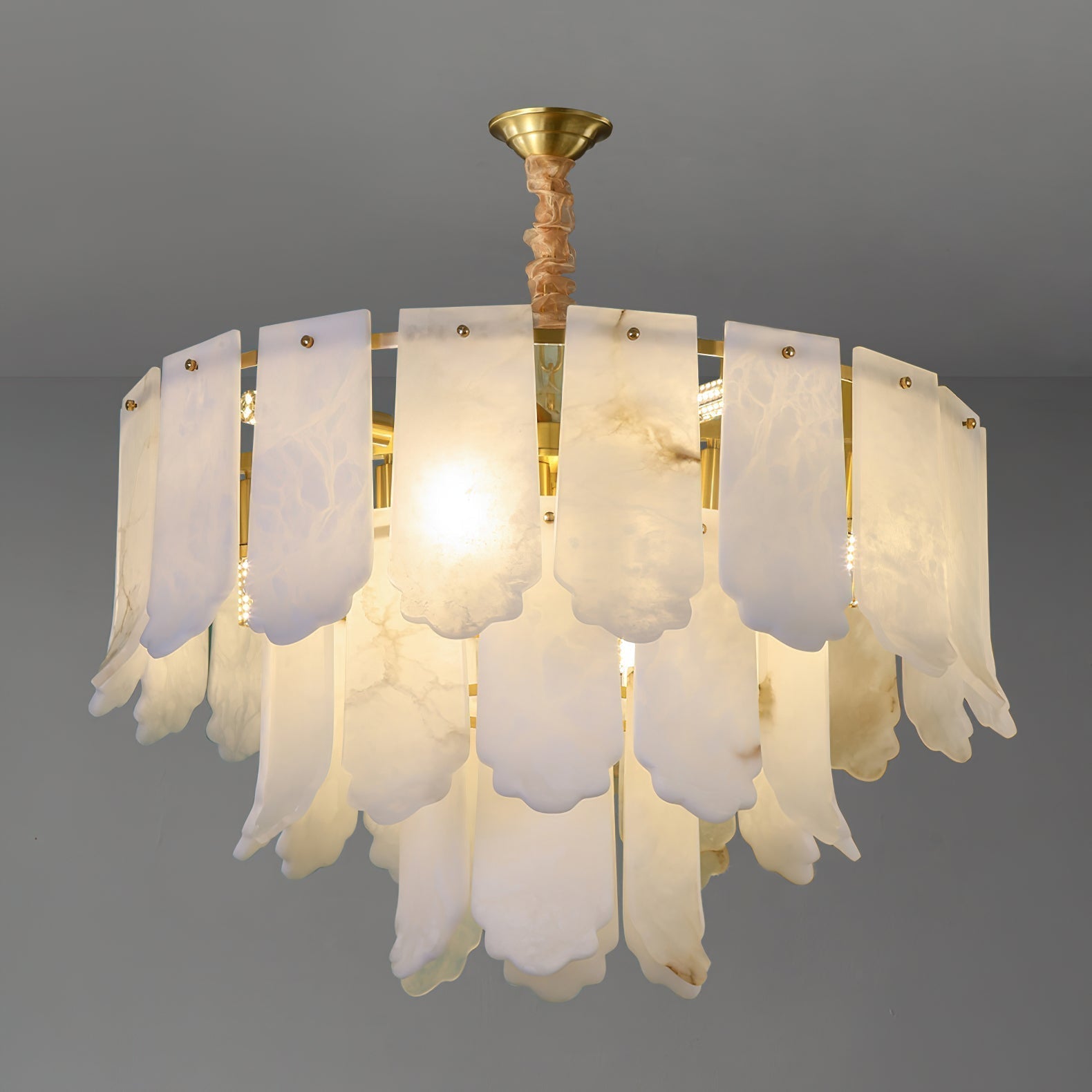 The Clérachic Hue Alabaster Chandelier lit on a grey studio ground, the heads reading as soft flares behind the stone plates.