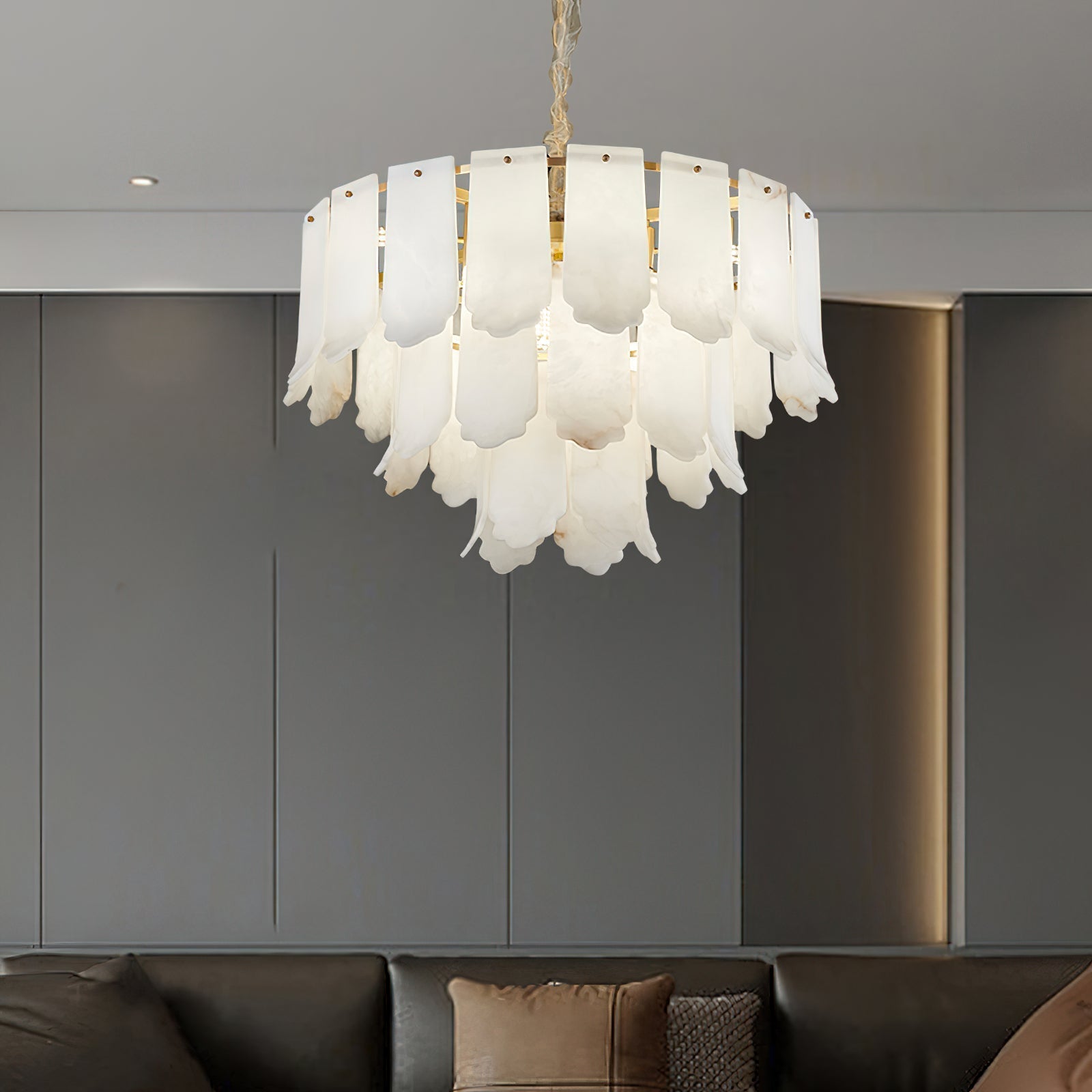 The Clérachic Hue Alabaster Chandelier hung against grey panelled joinery, its stone tiers lit above a dark sofa.