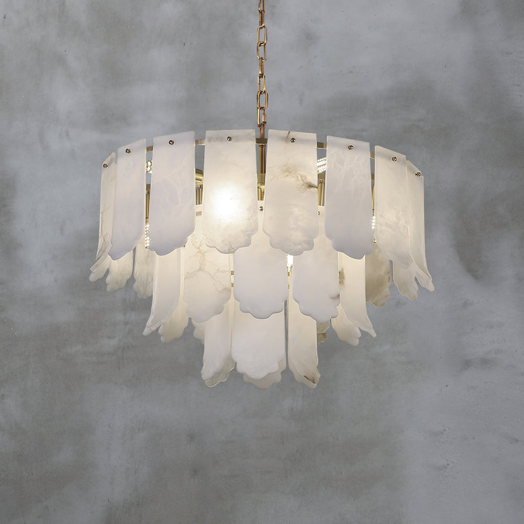 The Clérachic Hue Alabaster Chandelier lit on its brass chain against a bare concrete wall, veining showing through each plate.