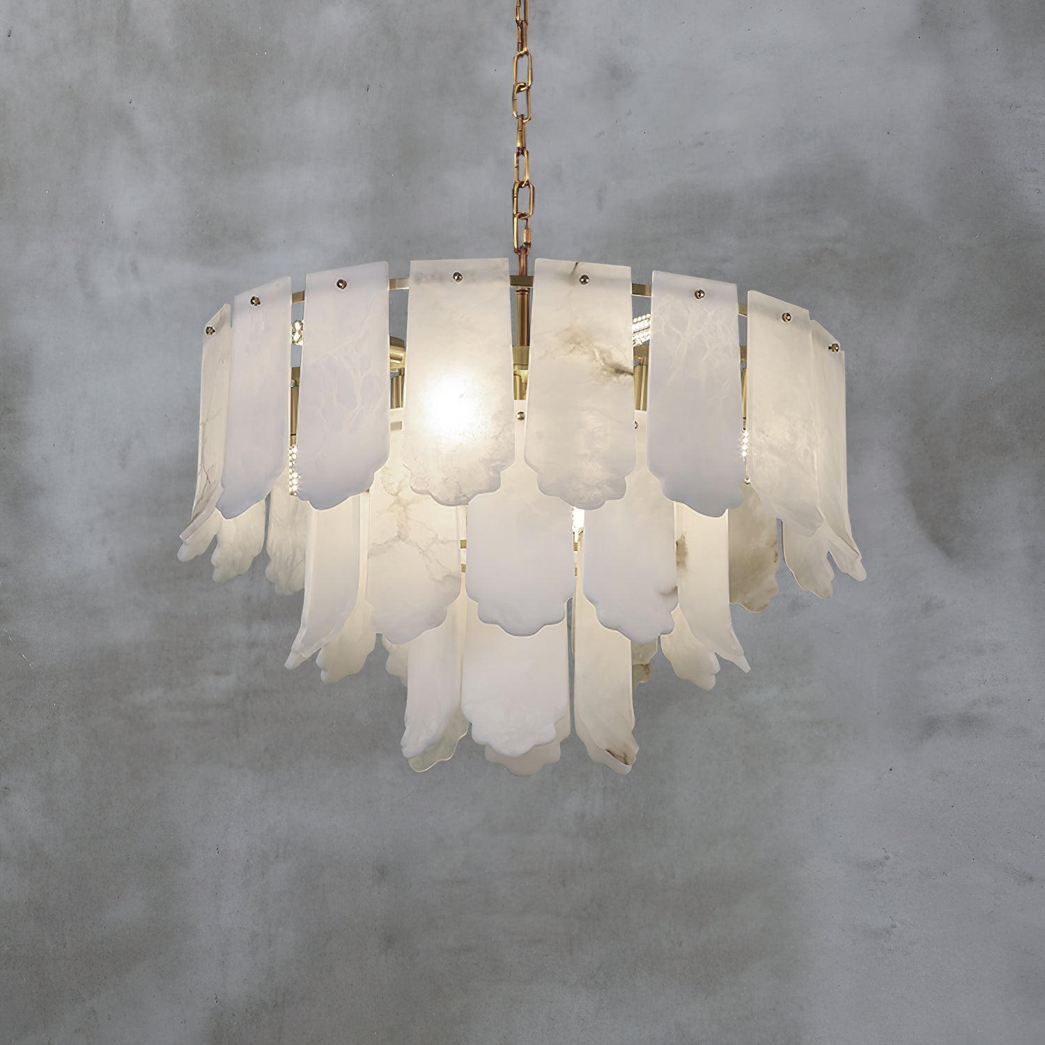 The Clérachic Hue Alabaster Chandelier lit on its brass chain against a bare concrete wall, veining showing through each plate.