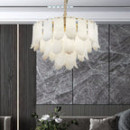 The Clérachic Hue Alabaster Chandelier lit before a grey marble feature wall, seen over a sofa and a vase of white blooms.