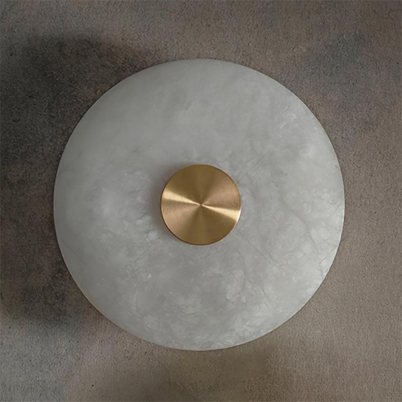 Clérachic alabaster disc sconce photographed at a slight angle, the brass hub catching light on a warm plaster wall.
