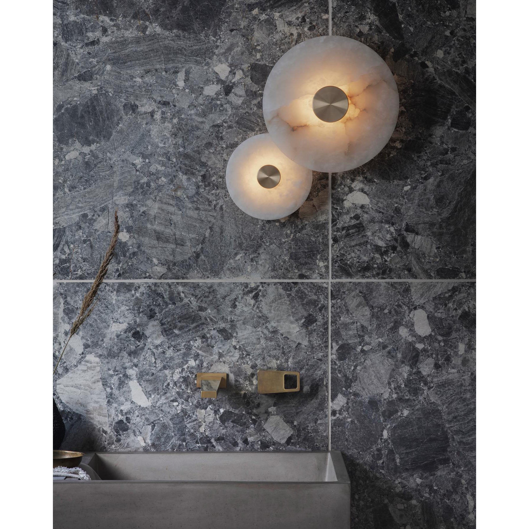 The Clérachic sconces in two sizes, lit above a stone basin on dark grey marble tiling in a bathroom.