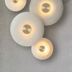 Clérachic sconces arranged as a group of four on a raw concrete wall, all lit, discs at staggered heights.