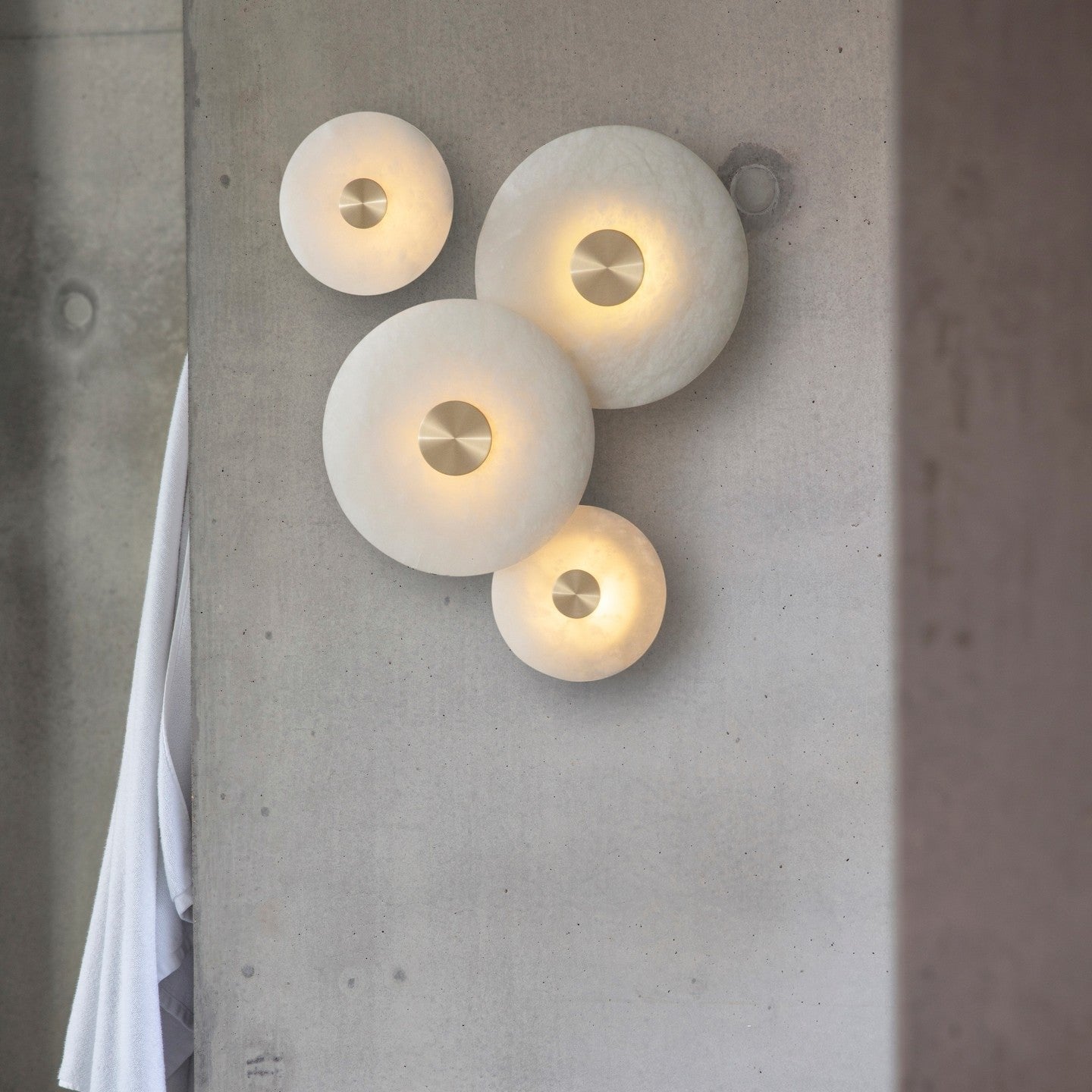 Four Clérachic discs clustered on a concrete column, lit warm, with a white curtain hanging alongside them.