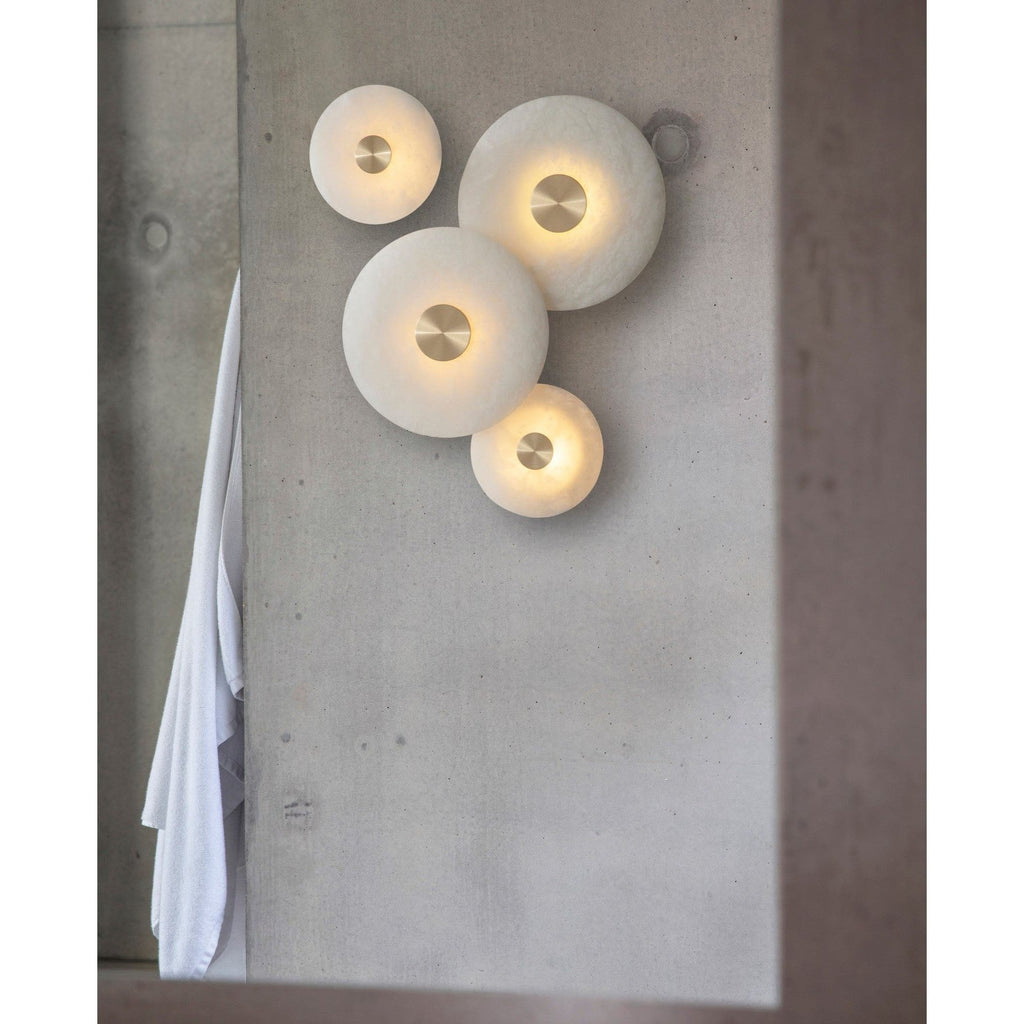 Clérachic wall lights grouped in mixed sizes on board-marked concrete, each glowing through its own alabaster disc.