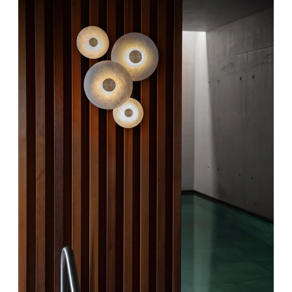 The Clérachic sconces mounted on a dark walnut slatted wall, four warm points of light along a concrete corridor.
