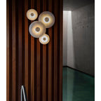 The Clérachic sconces mounted on a dark walnut slatted wall, four warm points of light along a concrete corridor.