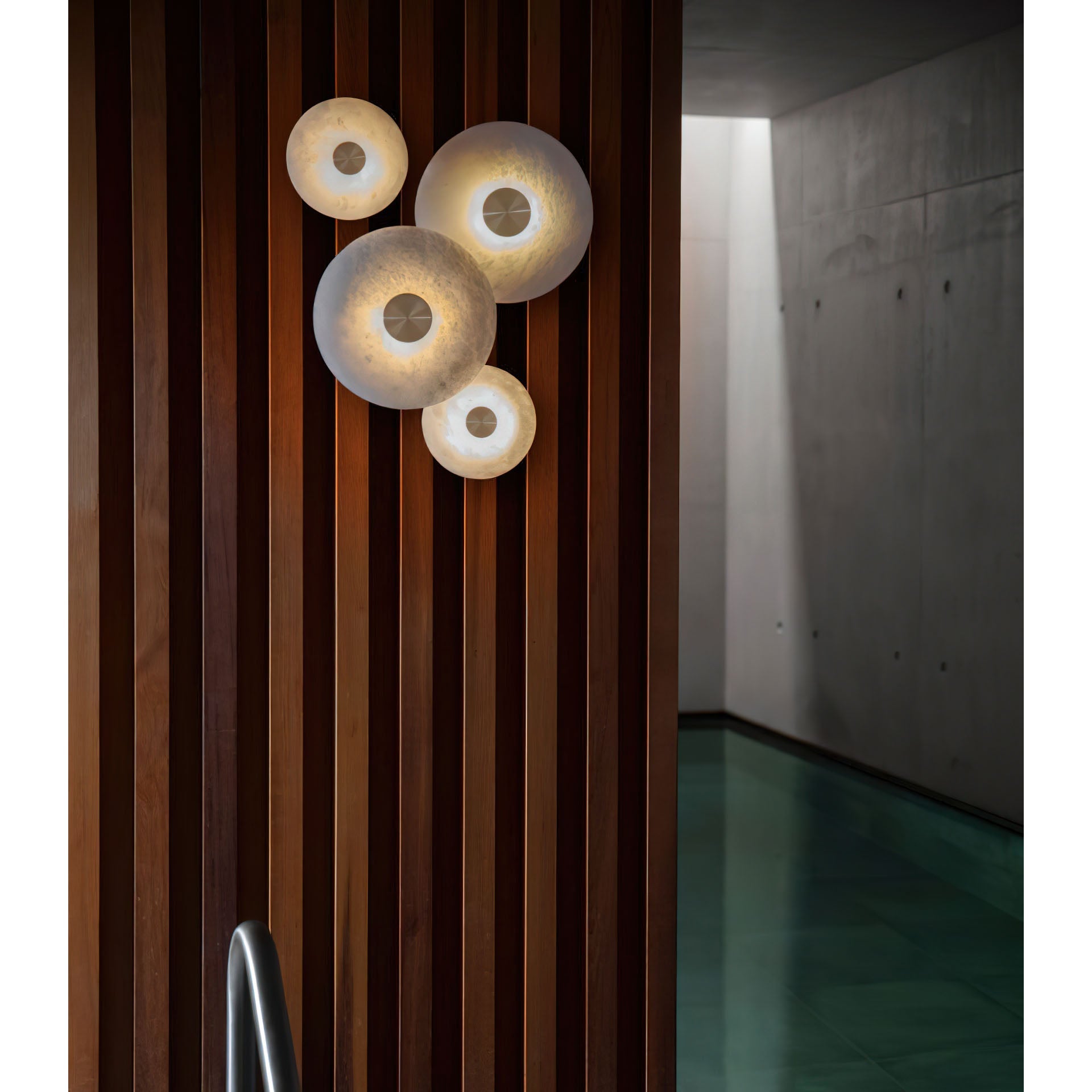 The Clérachic sconces mounted on a dark walnut slatted wall, four warm points of light along a concrete corridor.