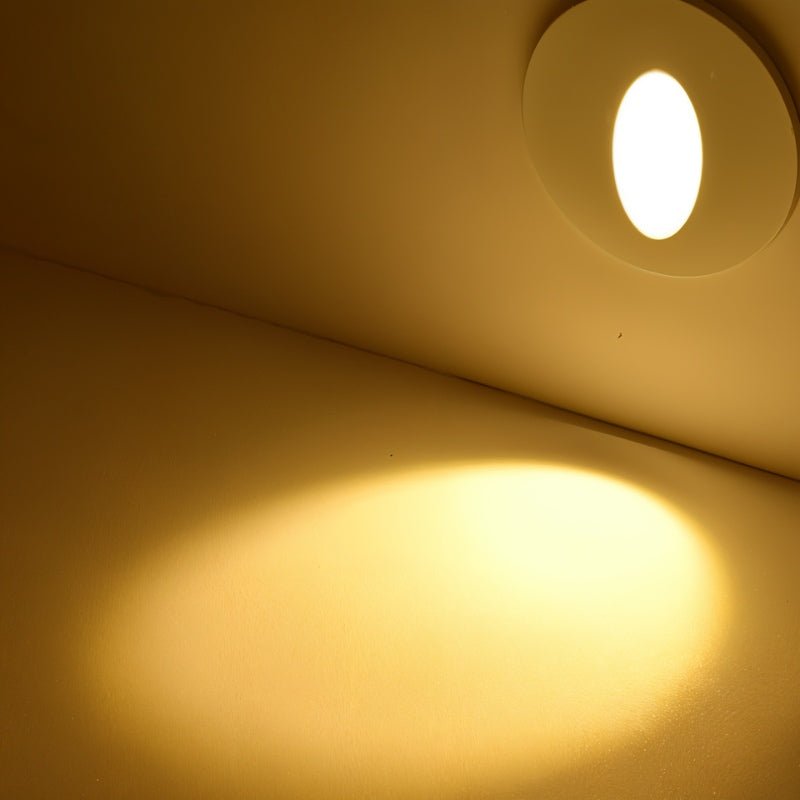 Clérachic white round stair light glowing warm on a wall, its light pooling in an oval across the surface below.