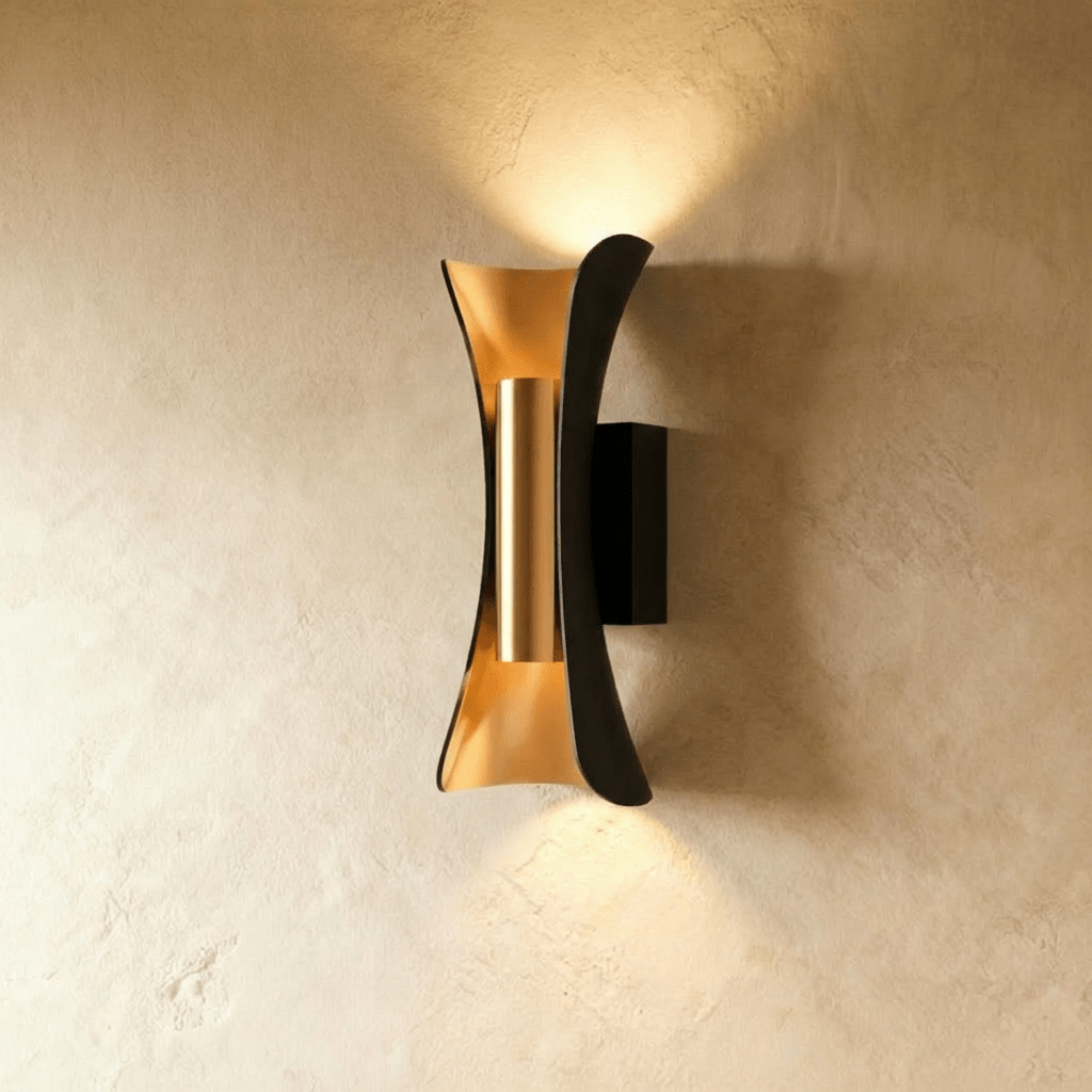 Clérachic black curved wall lamp with a brushed gold interior, throwing a warm beam up and down a textured wall.
