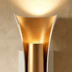 Close-up of the Clérachic white wall lamp, its brushed gold reflector curving around a gold cylinder and glowing upward.