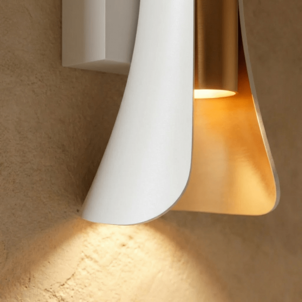 Close-up of the lower edge of the Clérachic white wall lamp, a gold cylinder lit beneath the curved white shell.