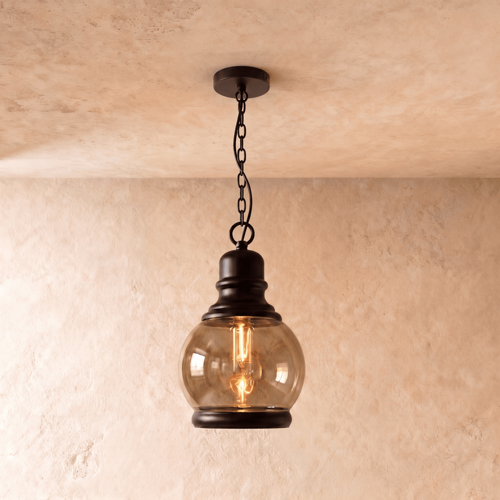 Clérachic pendant with a round amber-tinted glass globe and black iron cap, hung on a black chain, filament bulb glowing.