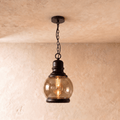 Clérachic pendant with a round amber-tinted glass globe and black iron cap, hung on a black chain, filament bulb glowing.