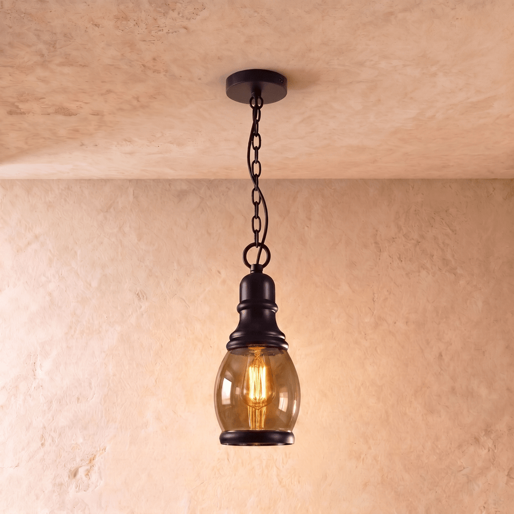 Clérachic tall oval amber glass pendant with a black iron cap and chain, glowing with a filament bulb on limewash.
