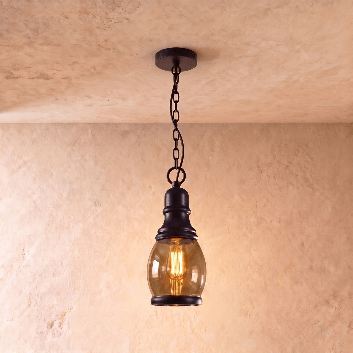 Clérachic tall oval amber glass pendant with a black iron cap and chain, glowing with a filament bulb on limewash.