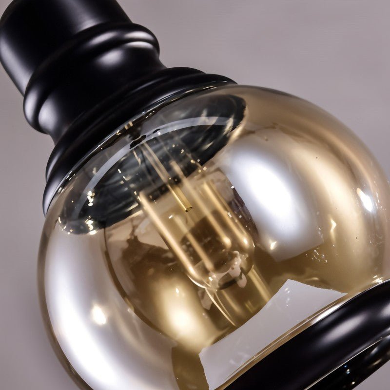 Close detail of a Clérachic round amber glass shade, black iron cap with turned rings, and the filament bulb inside.