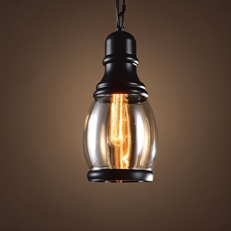 Clérachic tall oval clear-to-amber glass pendant with black iron cap and base ring, filament bulb lit on a dark backdrop.