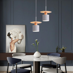 Clérachic pair of white saucer-and-drum pendants over a round marble table against a navy wall.