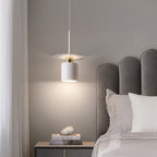 Clérachic white drum pendant with a gold neck over a grey nightstand beside a scalloped headboard.