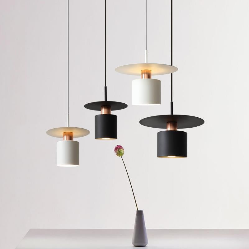 Clérachic black and white drum pendants with copper necks hanging at staggered heights on a grey backdrop.