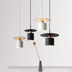 Clérachic black and white drum pendants with copper necks hanging at staggered heights on a grey backdrop.