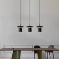 Clérachic three black drum pendants with copper trim in a row over a dark wood dining table.