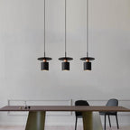 Clérachic three black drum pendants with copper trim in a row over a dark wood dining table.