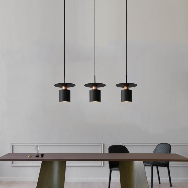 Clérachic three black drum pendants with copper trim in a row over a dark wood dining table.