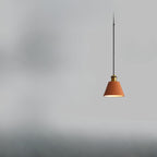 A Clérachic terracotta cone pendant hangs upper right on a black cord, brass cup against a hazy grey field.
