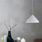 Clérachic white 1-light cone pendant with a wood neck, lit above blue and yellow vases on a grey wall.