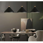 Three Clérachic black 1-light cone pendants hang in a row over a wood dining table and grey armchairs.