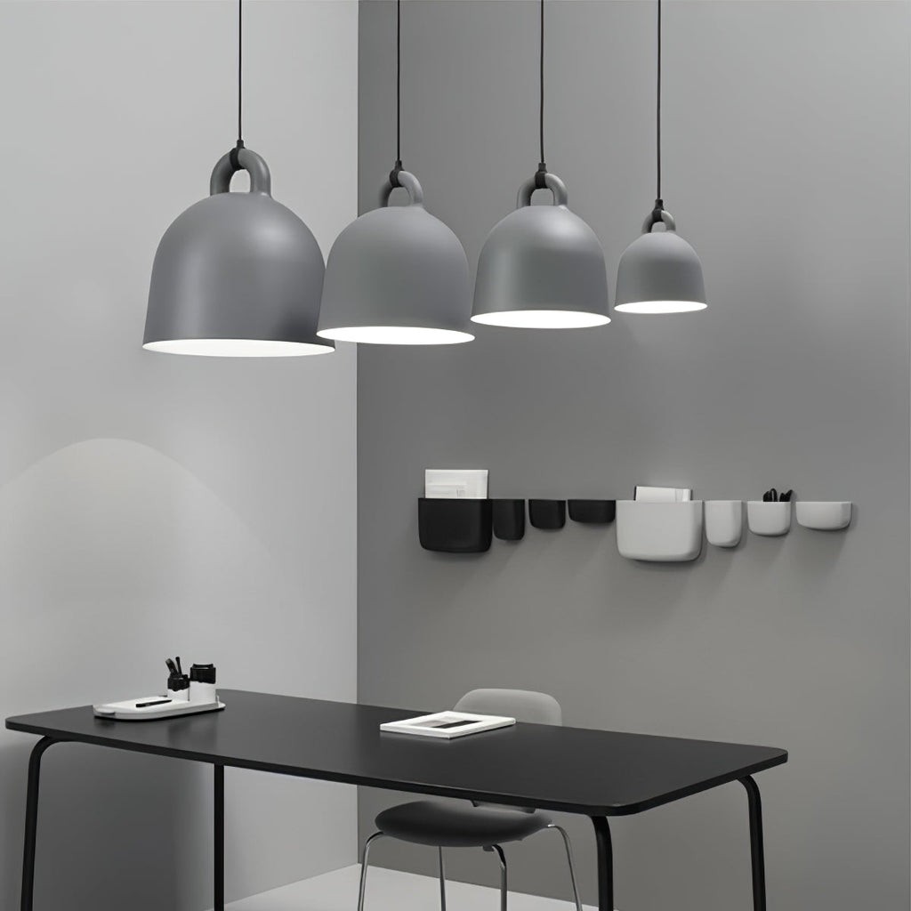 Four grey Clérachic bell pendants in graduated sizes hang over a black desk, with small wall pockets on the grey wall behind.
