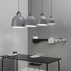 Four grey Clérachic bell pendants in graduated sizes hang over a black desk, with small wall pockets on the grey wall behind.