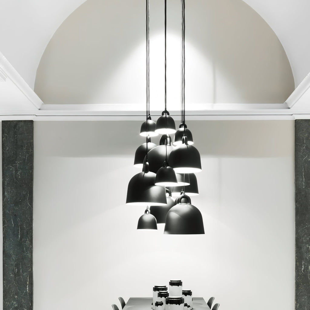 A cluster of black Clérachic bell pendants hangs at different heights in a tall, white arched room with dark green stone panels.