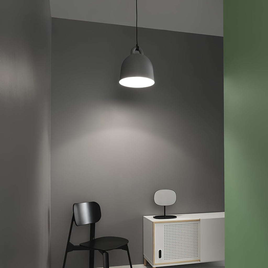 A single black Clérachic bell pendant glows on a dark grey wall, with a black chair and a small white cabinet below it.