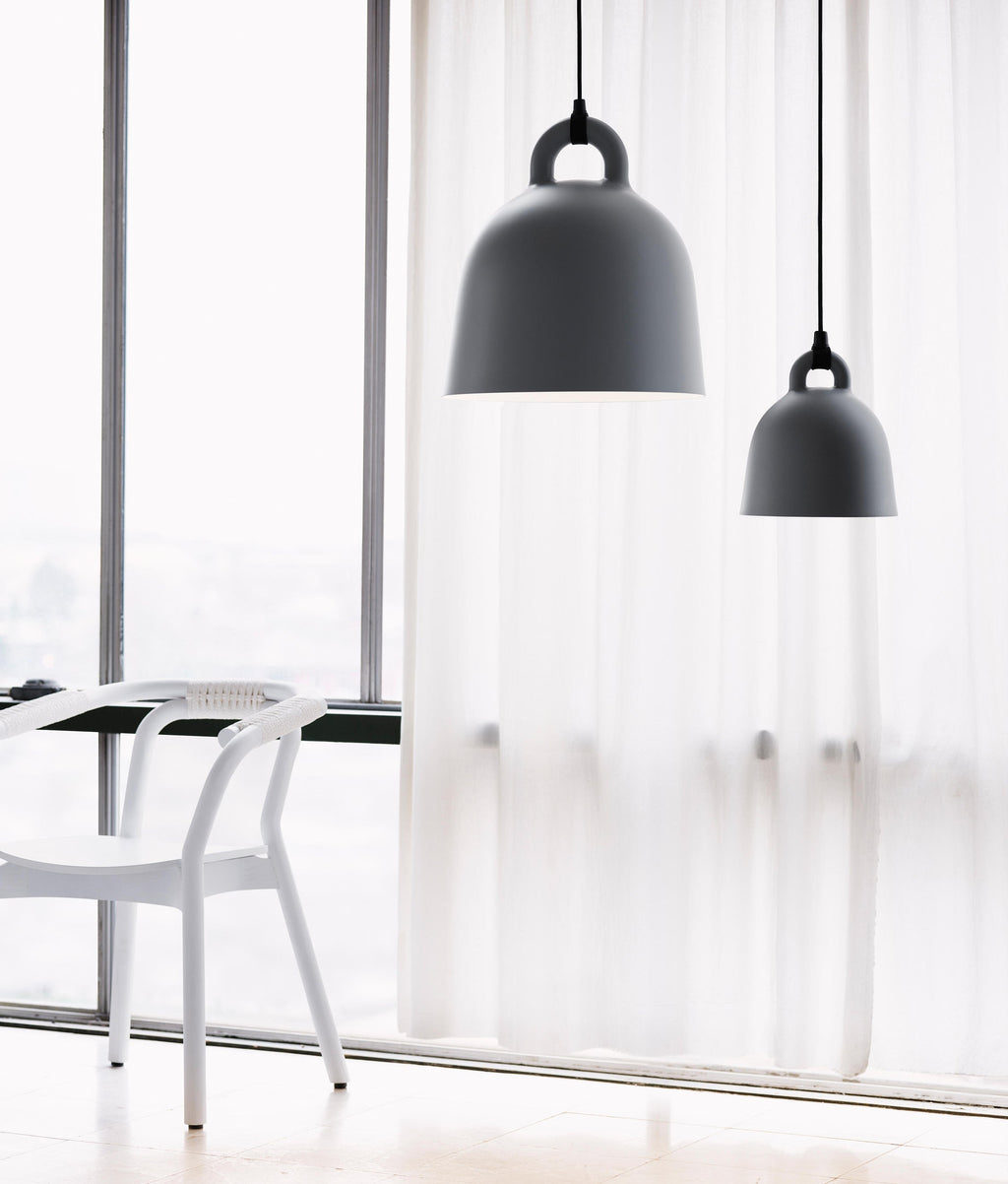 Two black Clérachic bell pendants in different sizes hang before a floor-length sheer curtain, with a white chair at the window.