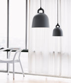Two black Clérachic bell pendants in different sizes hang before a floor-length sheer curtain, with a white chair at the window.