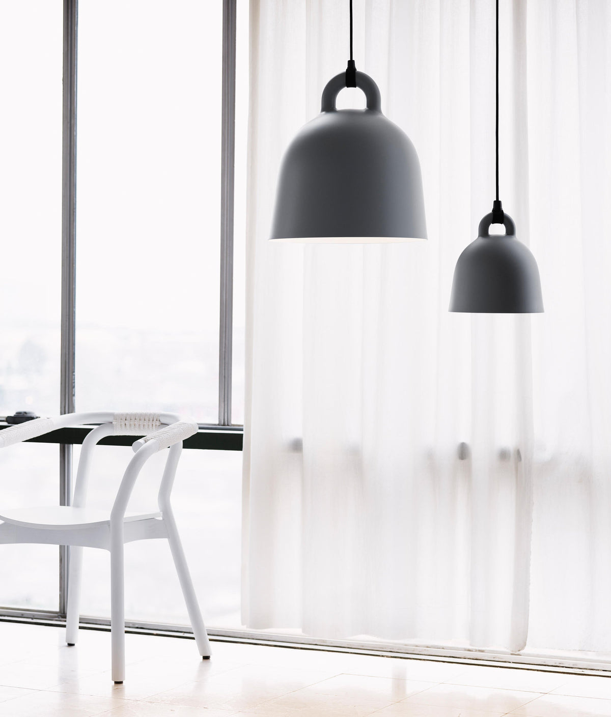 Two black Clérachic bell pendants in different sizes hang before a floor-length sheer curtain, with a white chair at the window.