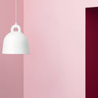 A white Clérachic bell pendant on a pink wall, cropped at the edge of the frame beside a deep red door.
