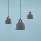 Three grey Clérachic bell pendants in different sizes float against a plain pale blue backdrop.
