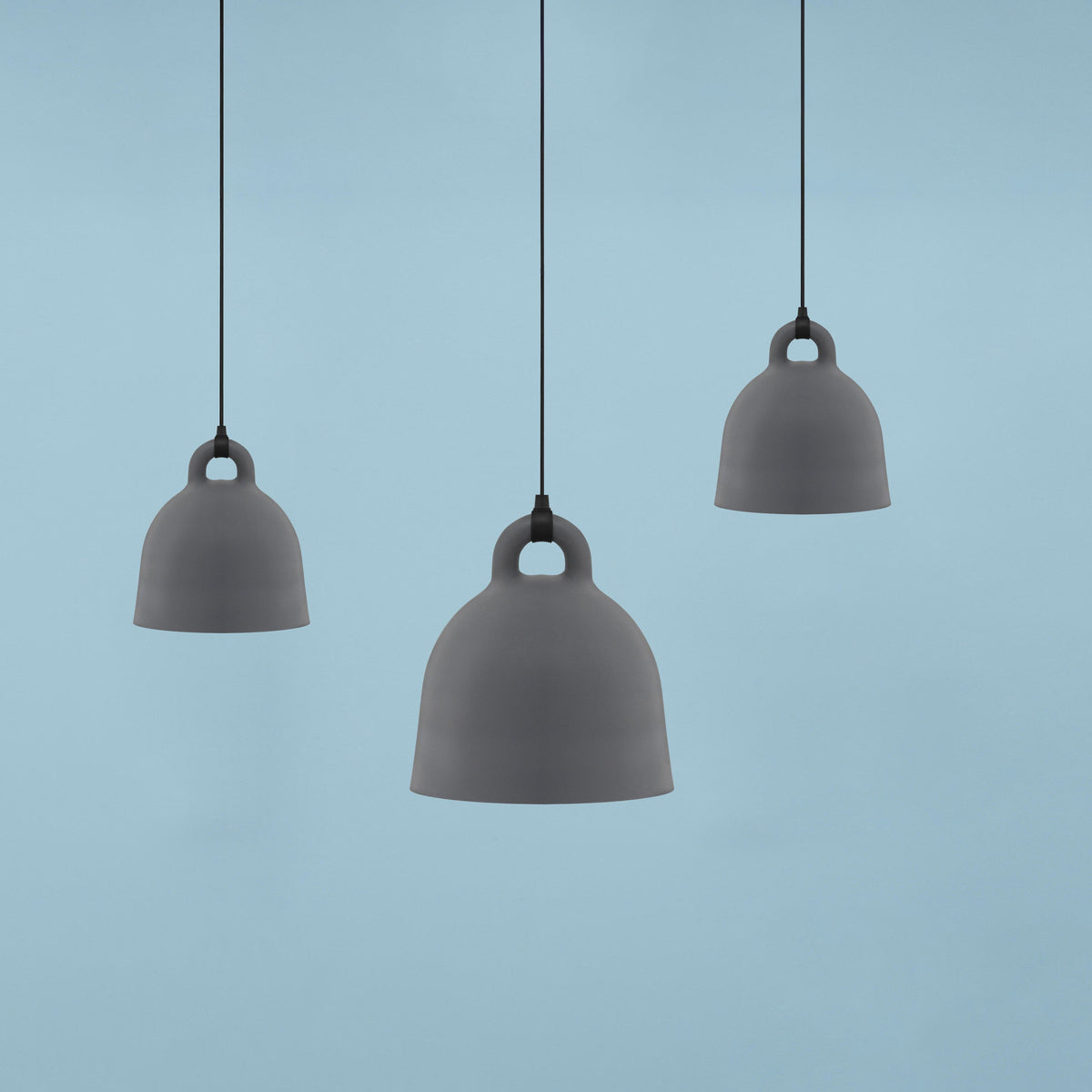 Three grey Clérachic bell pendants in different sizes float against a plain pale blue backdrop.
