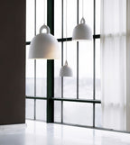White and grey Clérachic bell pendants hang in front of a tall black-framed window, with a sheer curtain to the right.