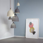 A group of grey Clérachic bell pendants hangs in a blue-grey corner, beside a framed abstract print leaning on the floor.