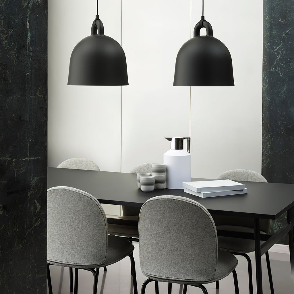 Two large black Clérachic bell pendants hang over a black dining table with grey shell chairs, beside dark green marble.