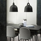 Two large black Clérachic bell pendants hang over a black dining table with grey shell chairs, beside dark green marble.