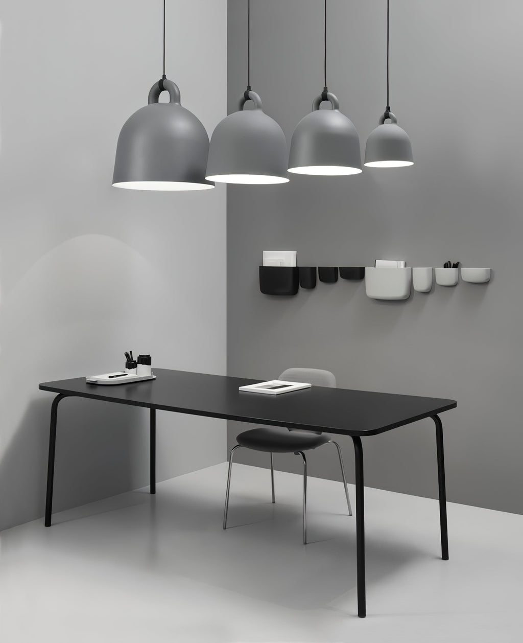 Four grey Clérachic bell pendants, graduated in size, hang over a black table, with wall pockets on the grey corner wall.