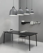 Four grey Clérachic bell pendants, graduated in size, hang over a black table, with wall pockets on the grey corner wall.